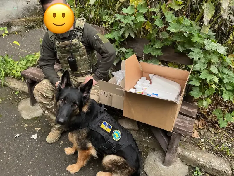 Dana beside a person in uniform and a box of supplies